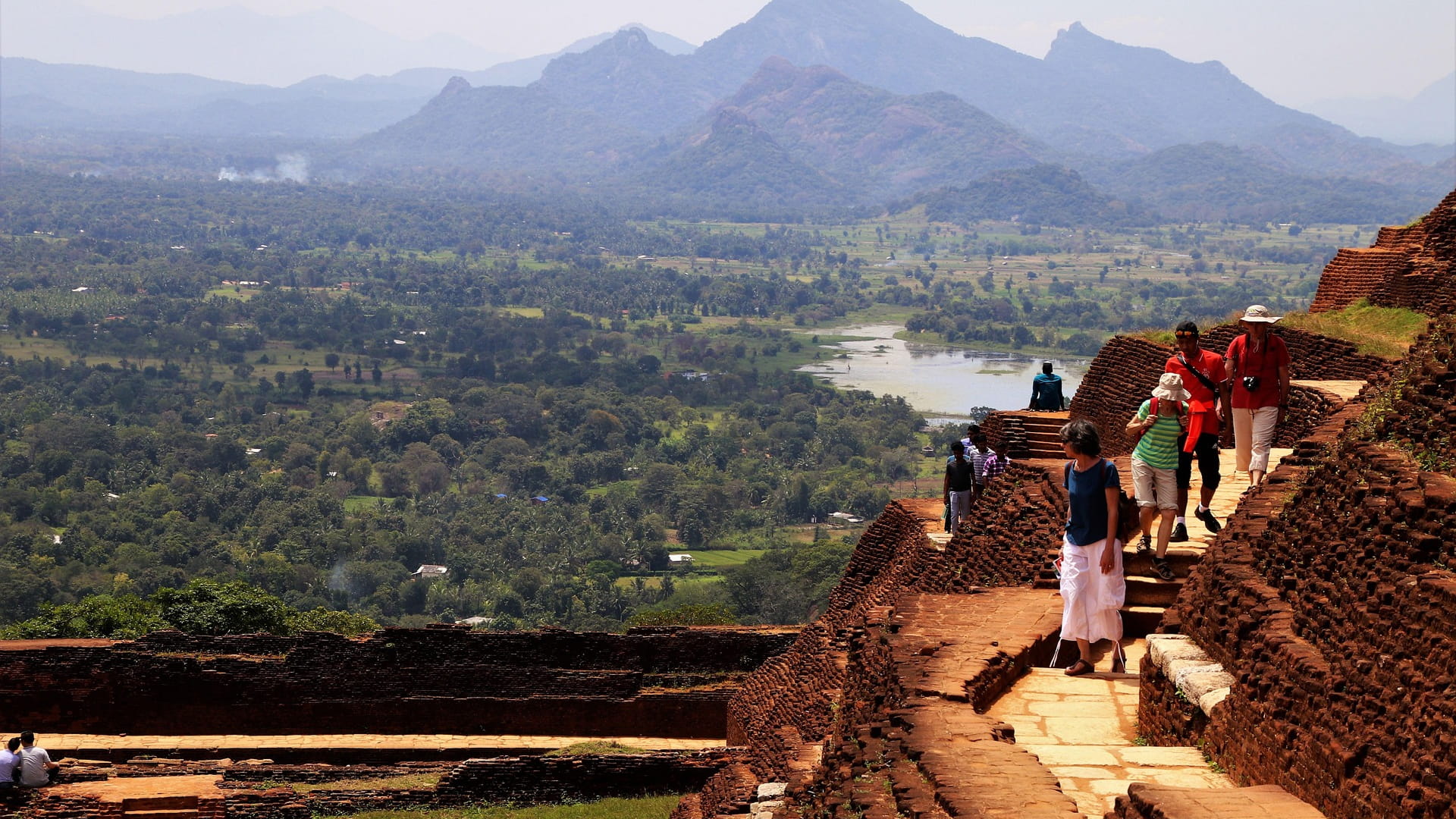 Tourists and locals atop the Sigiriya rock fortress with beautiful hills in the background