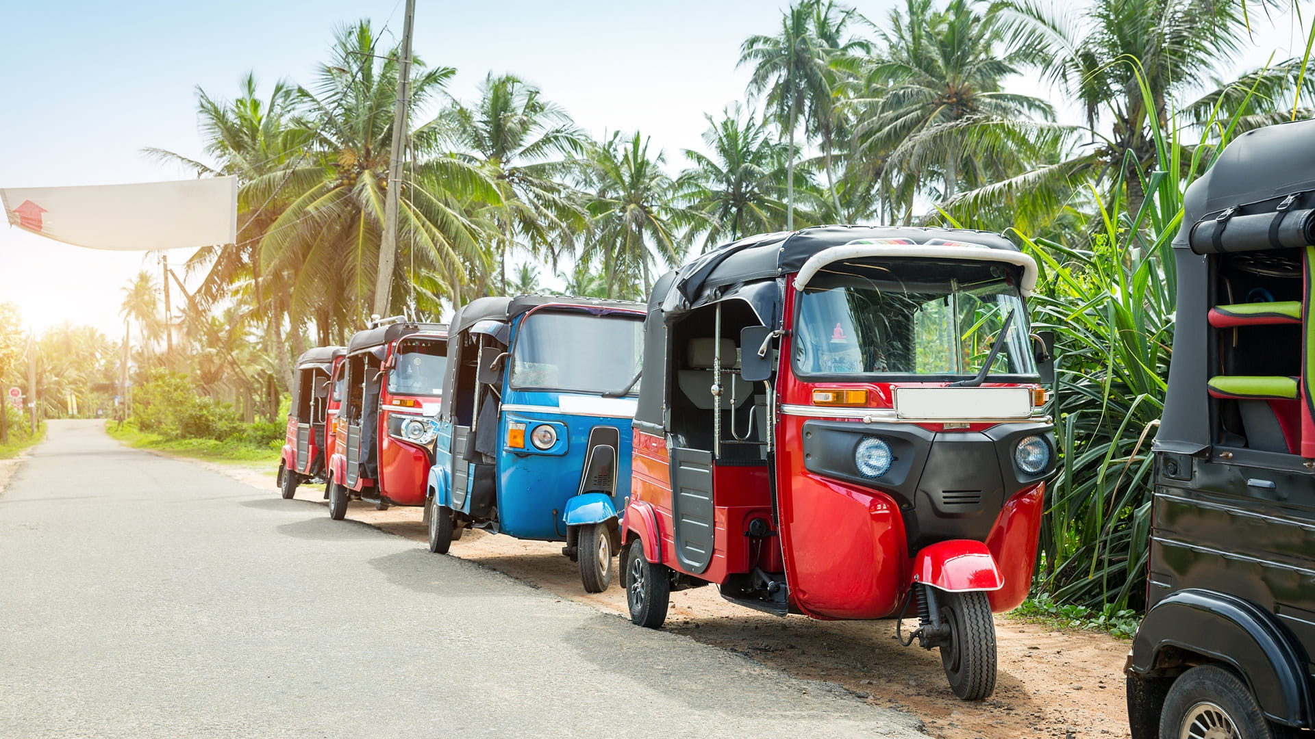 A row of colourful three wheeled vehicles lined up on the road