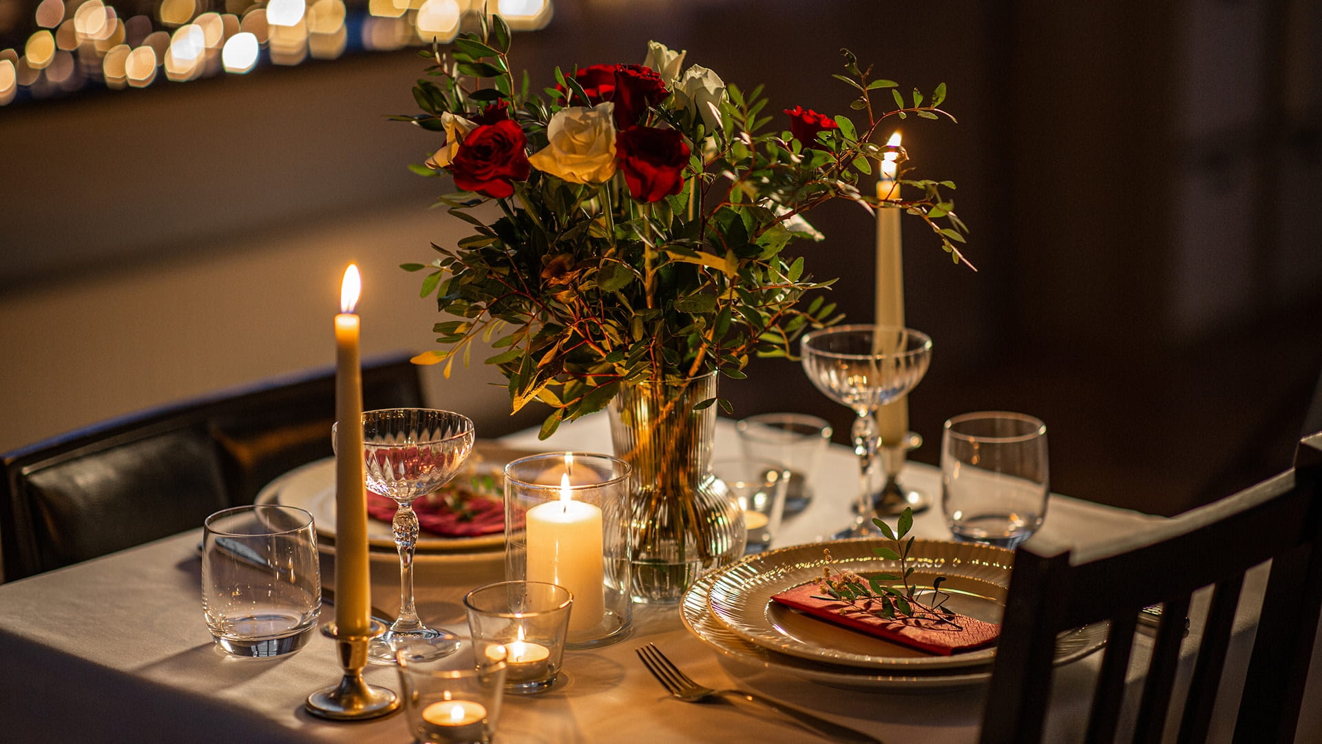 A beautifully set up romantic dinner table for 2 decorated with red and white roses and candles