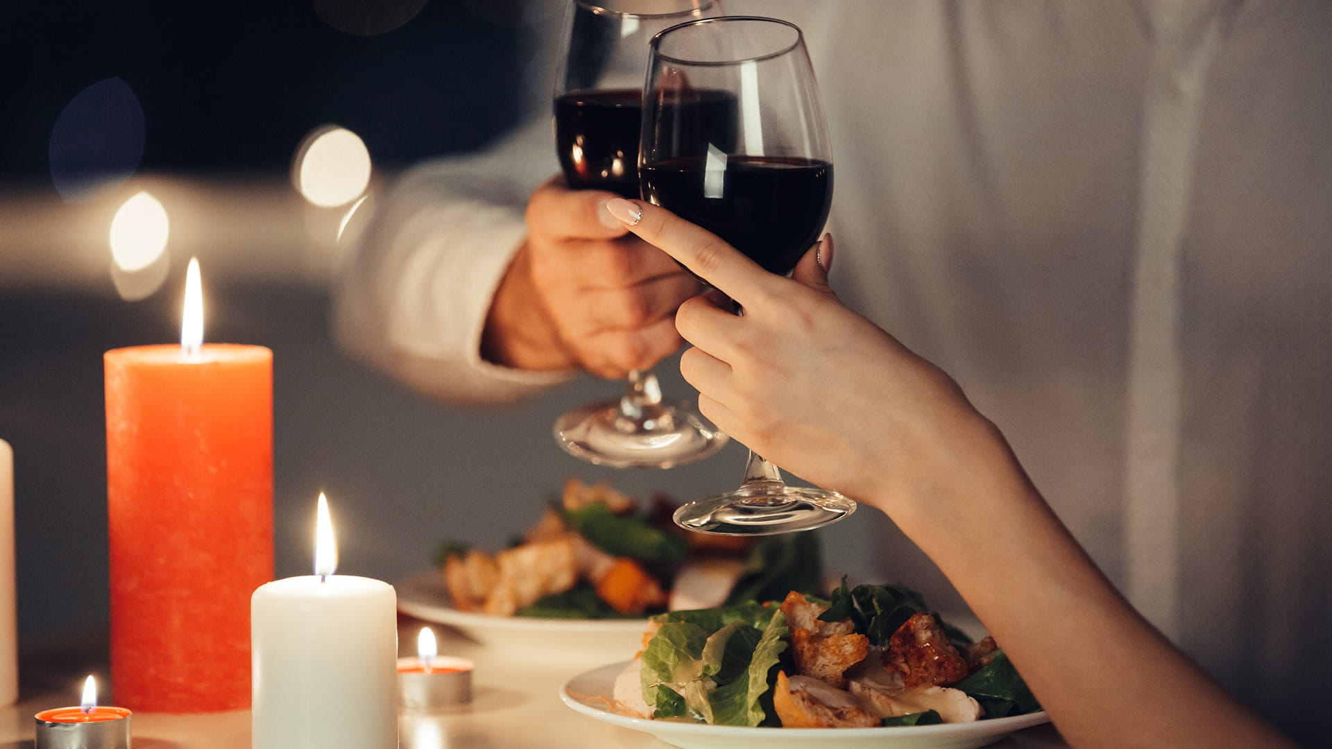 A couple clinking their glasses of wine at a romantic dinner with candles