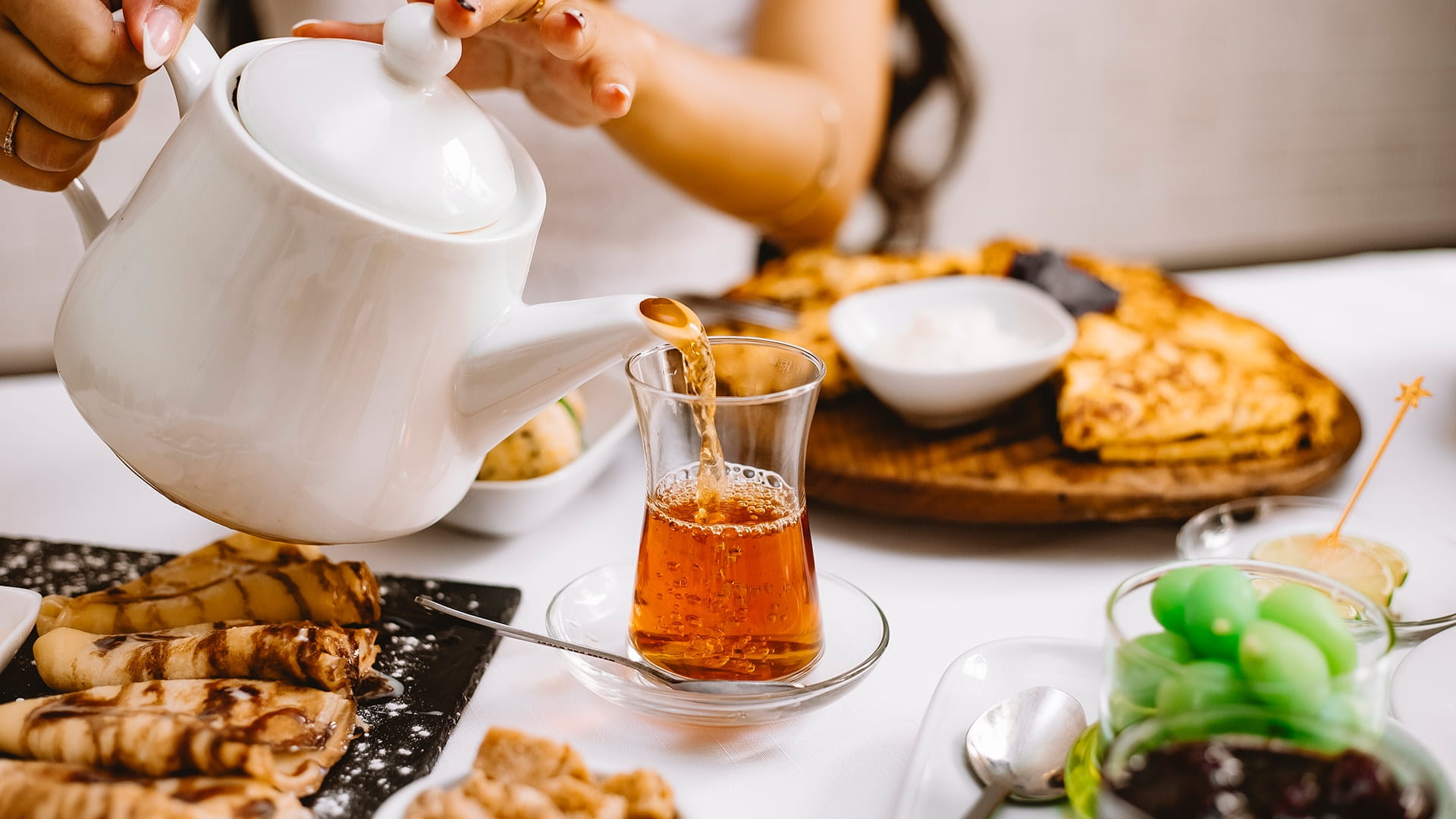 Tea being served in a clear glass with sweet treats laid at the table 